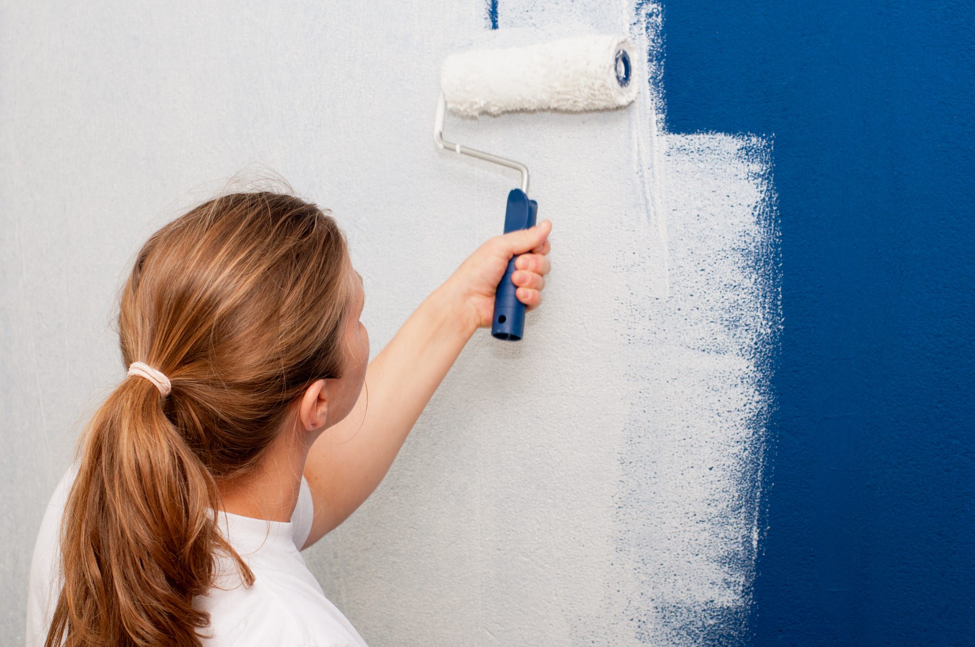 Woman painting interior wall of house with a roller